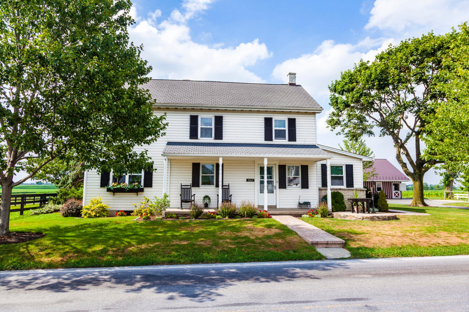 A two-story home with white siding, on a large, rural property.