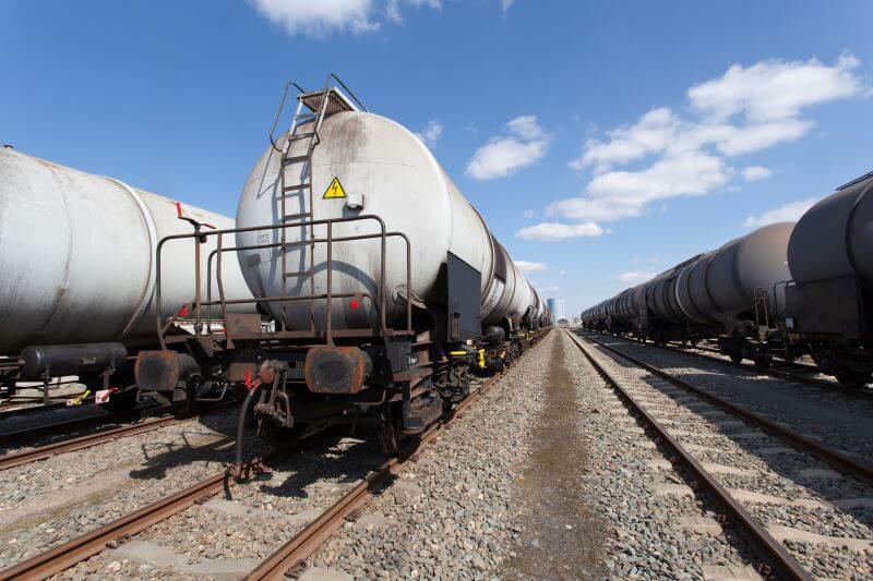 A photo of a rail yard with propane tanks on rail cars. There is a blue sky with clouds.